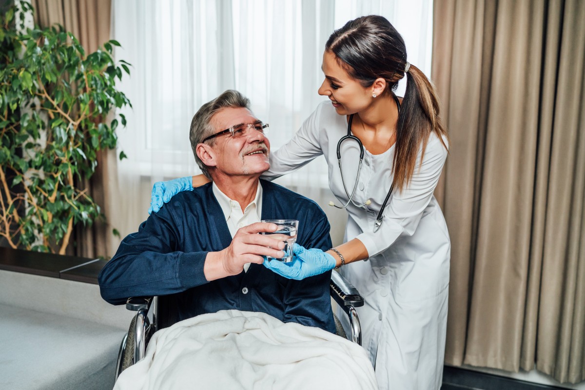 older man wheelchair smiles nurse assistant she hands him glass water (1)